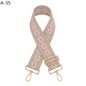 Detail view of ethnic style woven geometric bag strap in beige and pink with gold hooks