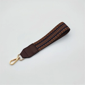 Macro view of geometric jacquard bag strap with brown leather and gold lobster clasp