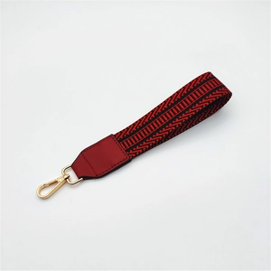 Close-up of woven bag strap with red and black geometric patterns and gold metal clasp