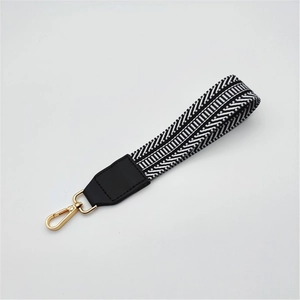 Detail of woven black and white handbag strap with golden lobster clasp and leather trim
