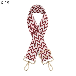 Detail of red and white geometric jacquard bag strap with gold metal hooks and buckle