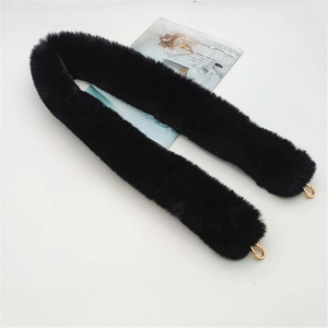 Detail of black faux fur bag strap with gold metal lobster clasps on a white surface