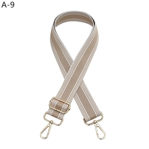Detail of wide adjustable khaki and white striped bag strap with gold metal hardware