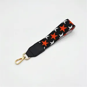 Detail of black woven wrist strap with orange and white stars and golden lobster clasp