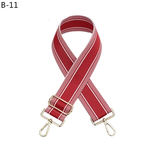 Close-up of adjustable wine red polyester bag strap with white stripes and gold buckles