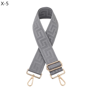 Close-up of gray woven bag strap with geometric jacquard pattern and gold metal hooks