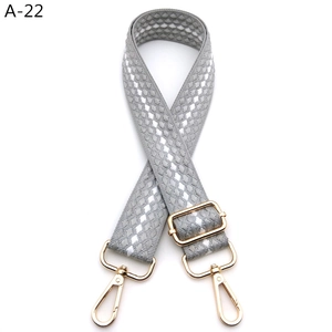 Close-up of gray woven bag strap with silver diamond pattern and gold metal buckles