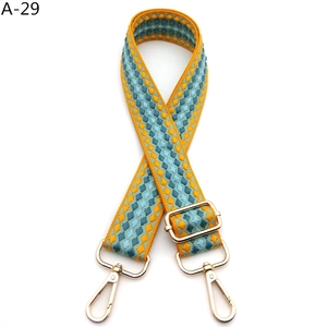 Detail view of woven diamond pattern bag strap with gold metal hooks and adjustable buckle