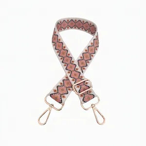 Detail view of ethnic style woven bag strap with pink geometric patterns and gold buckles