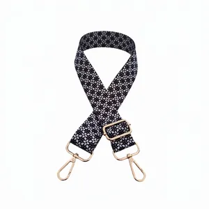 Detail of adjustable floral woven bag strap with golden buckles and black flower pattern