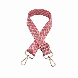 Detail of adjustable coral pink canvas bag strap with white flower pattern and gold hooks