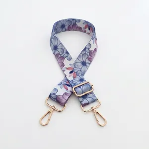 Detail of adjustable wide woven bag strap with purple floral prints and gold metal hooks
