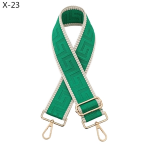 Detail of green and beige geometric woven bag strap with polished gold-tone metal hardware