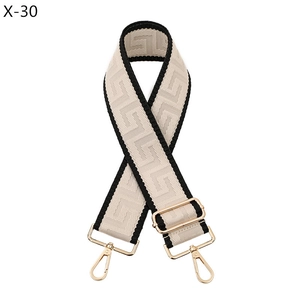 Close-up of wide woven bag strap with Greek key pattern and gold metal swivel hooks