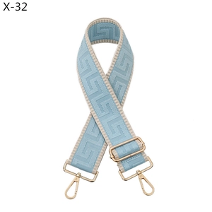 Detail of light blue wide bag strap with geometric pattern and gold-tone metal hardware
