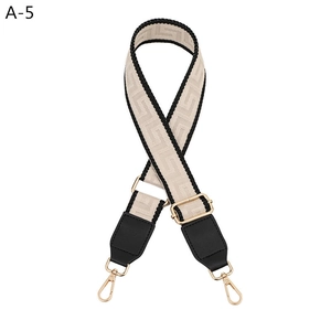 Close-up of beige Greek Key pattern bag strap with black leather ends and gold hardware