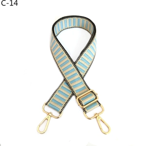 Detail of adjustable woven bag strap featuring light blue stripes and gold metal hardware
