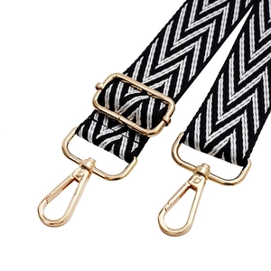 Detail view of woven black and white wave pattern bag strap with gold metal buckles
