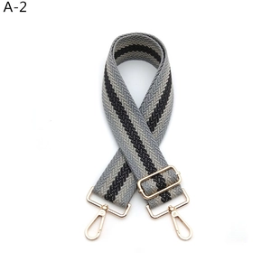 Detail of adjustable wide canvas shoulder strap with grey stripes and gold metal hardware