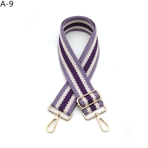 Close-up of a wide woven purple and beige adjustable bag strap with gold metal hooks