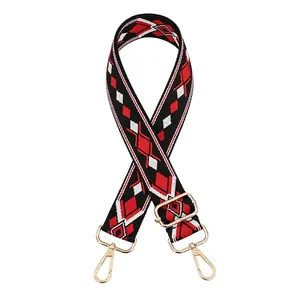 Detail of jacquard bag strap with red and black geometric patterns and gold metal buckles