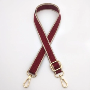 Detail of red jacquard woven bag strap with golden metal swivel hooks and adjustable buckle