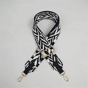 Detail of adjustable geometric jacquard bag strap with gold metal hooks and black leather