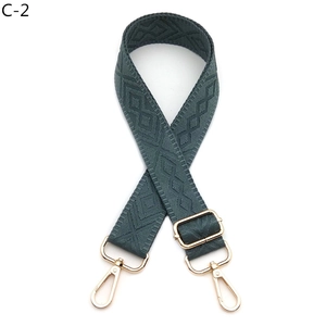 Close-up of deep green diamond pattern woven bag strap with golden metal lobster clasps