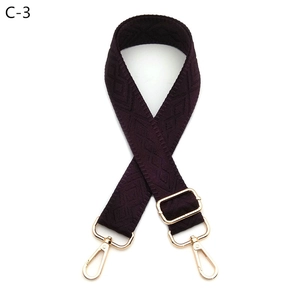 Close-up of deep purple woven bag strap with golden metal lobster clasps and geometric pattern