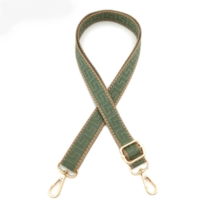 Detail of adjustable woven bag strap with green geometric patterns and gold metal hooks