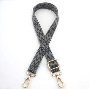 Macro view of adjustable woven bag strap with grey geometric patterns and gold lobster clasps