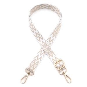 Detail of adjustable beige woven bag strap with geometric patterns and gold metal hooks
