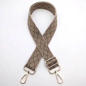 Detail of adjustable woven bag strap with beige geometric pattern and gold buckles