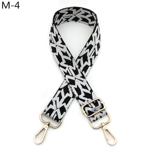 Detail of adjustable woven bag strap featuring black and white chevron patterns and gold buckles