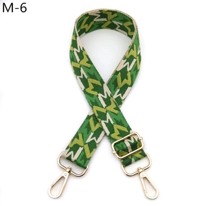 Adjustable woven shoulder strap featuring green geometric patterns and gold metal hooks