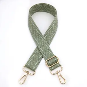 Detail of light green woven bag strap with white chevron pattern and gold metal hooks