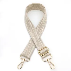 Detail of beige woven bag strap with herringbone pattern and gold rotating metal hooks