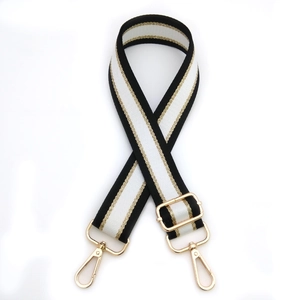 Macro shot of wide black, white and gold metallic striped bag strap with gold lobster clasps