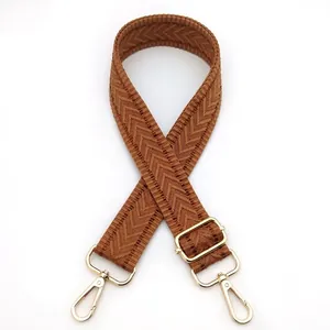 Detail view of brown herringbone woven strap with shiny gold lobster clasps and metal buckle