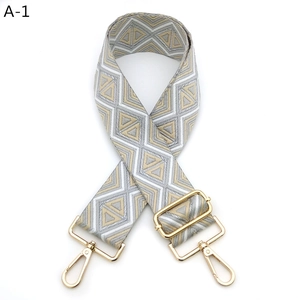 Detail of adjustable wide woven bag strap with geometric patterns and gold lobster clasps