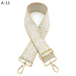 Close-up of wide jacquard strap with geometric pattern and gold swivel snap hooks