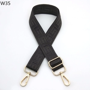 Detail of adjustable black bag strap with embossed Greek key pattern and gold metal hooks