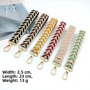 Detail of leaf pattern embroidered wrist straps with golden metal D-rings and rivets