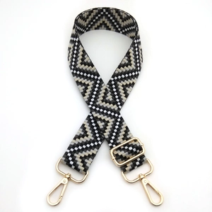 Detailed view of woven geometric bag strap in black and gold with metal hooks