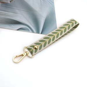 Close-up of beige leaf pattern fabric wrist strap with golden lobster clasp and metal rivet