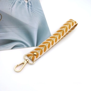 Close-up of beige leaf embroidery wristlet strap with gold lobster clasp and rivets