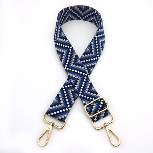 Detail of adjustable woven bag strap with blue geometric patterns and gold metal hooks