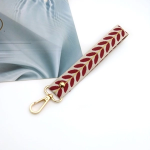 Detail of leaf pattern wrist strap with gold metal lobster clasp and cream woven fabric