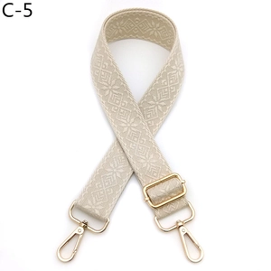 Close-up of adjustable beige embroidered bag strap with geometric patterns and gold clips