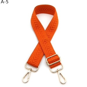 Close-up of bright orange woven shoulder strap with gold metal hooks and arrow pattern